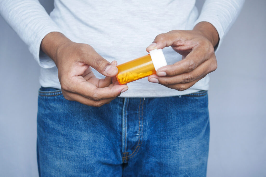 young man hand holding medicine orange and white color pill container