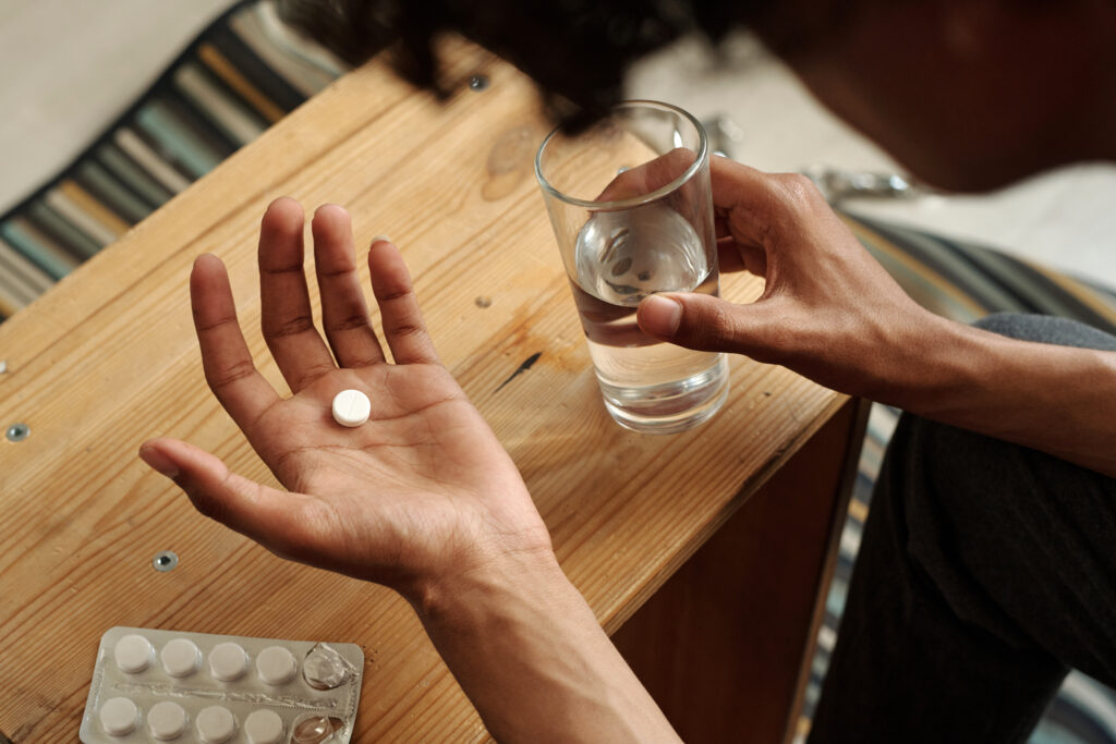 Above view of open palm of young man holding pill over small wooden table before dissolving it in glass of water