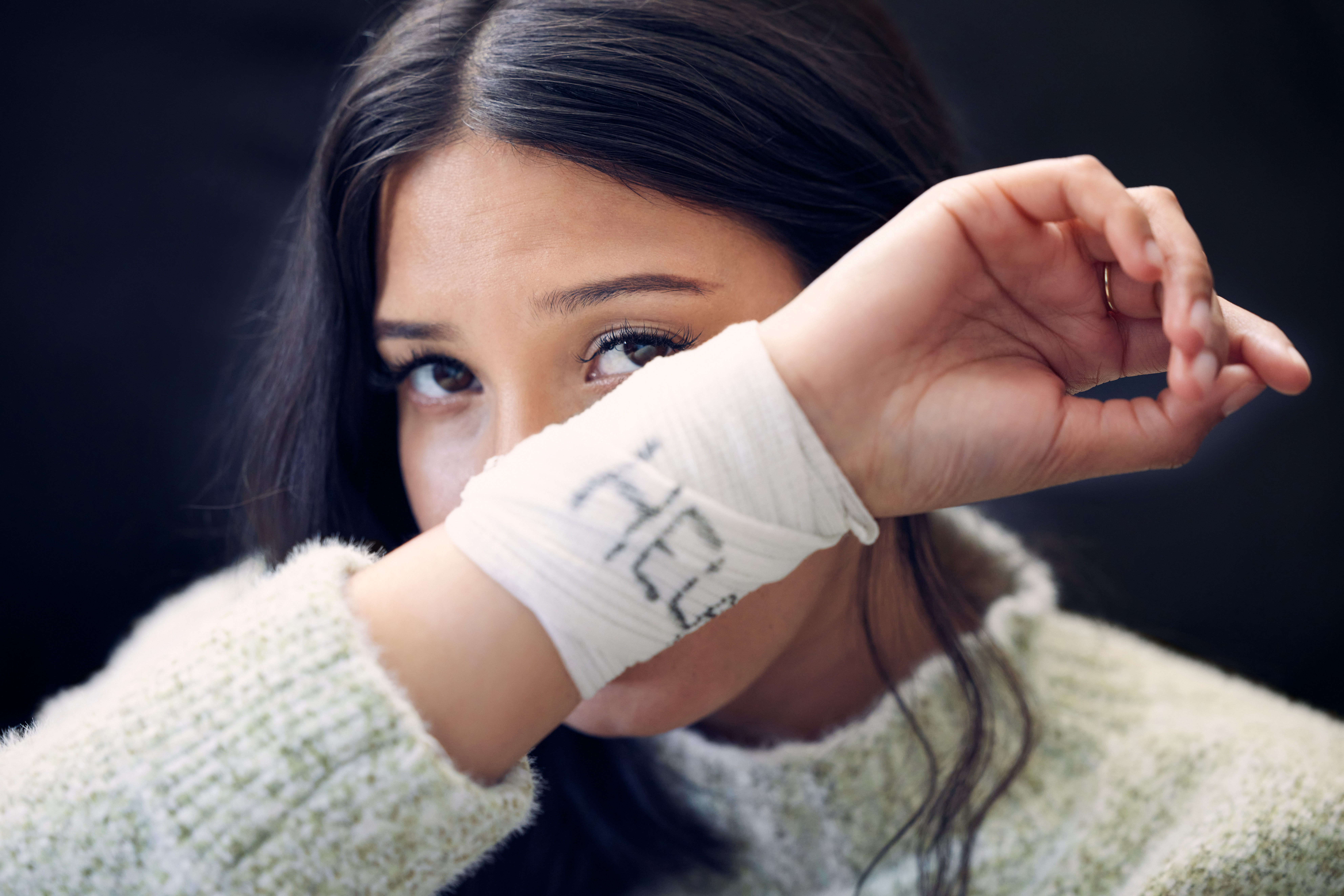 Shot of a young woman with bandages wrapped around her wrists showing help written on them.